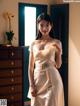 A woman in a white dress standing in front of a dresser.